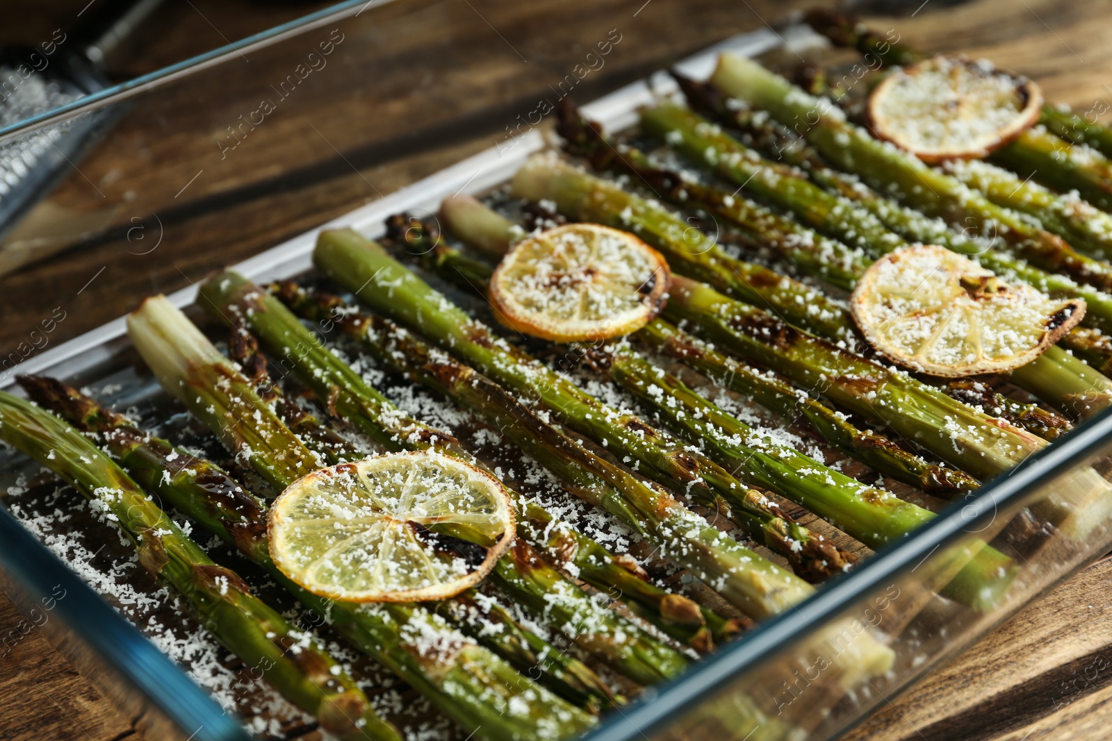 Photo of Oven baked asparagus with lemon slices in glass dish on table, closeup