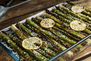 Oven baked asparagus with lemon slices in glass dish on table, closeup