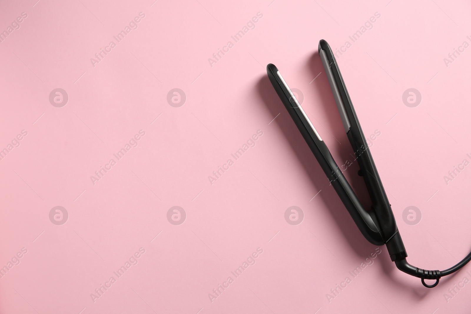 Photo of Modern flat hair iron on pink background, top view. Space for text