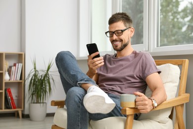 Photo of Happy handsome man using smartphone at home