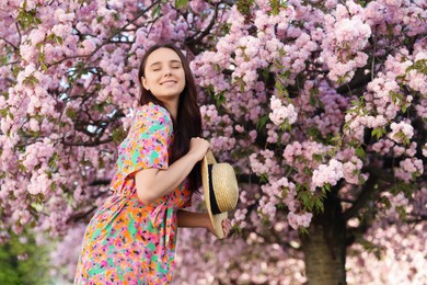 Beautiful woman with straw hat near blossoming tree on spring day