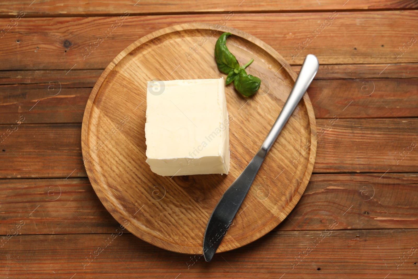 Photo of Block of tasty butter, knife and basil on wooden table, top view