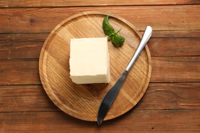 Block of tasty butter, knife and basil on wooden table, top view