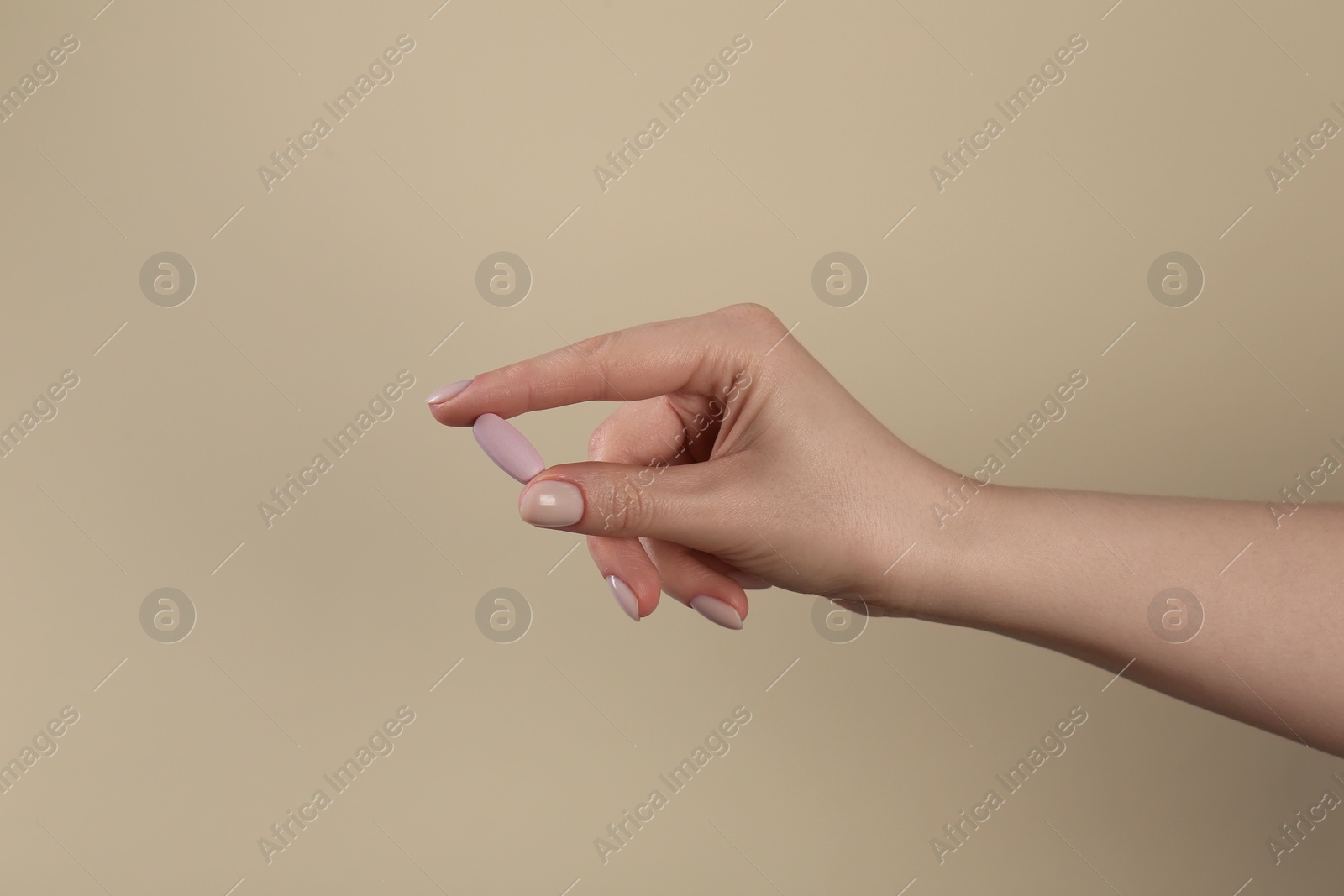 Photo of Woman holding vitamin pill on dark beige background, closeup. Health supplement