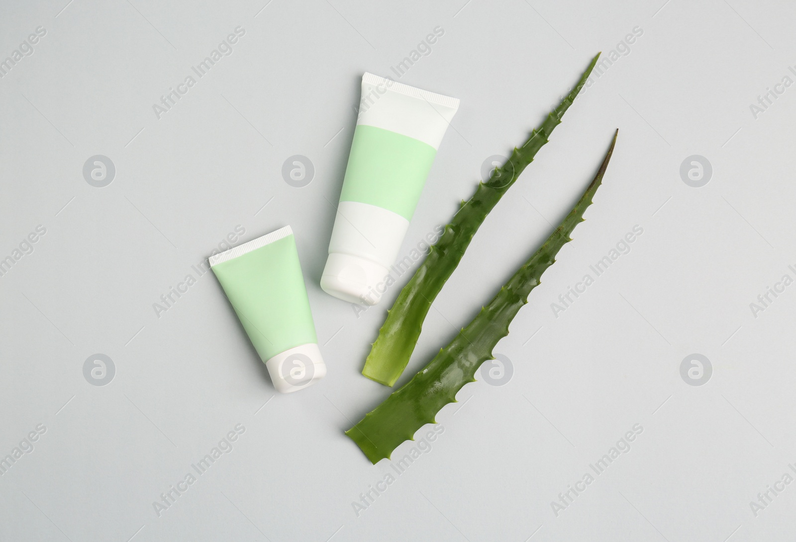 Photo of Tubes of toothpaste and fresh aloe on light grey background, flat lay