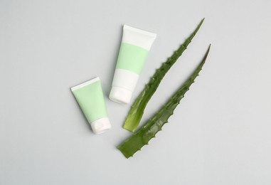 Tubes of toothpaste and fresh aloe on light grey background, flat lay