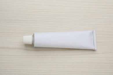 Photo of Blank white tube of ointment on light wooden table, top view. Space for text