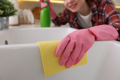 Photo of Woman cleaning kitchen sink with microfiber cloth at home, closeup