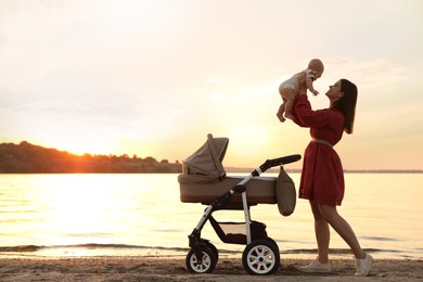 Happy mother with baby near river at sunset