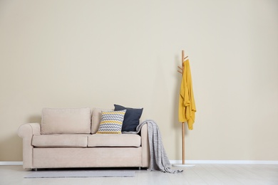 Minimalist living room interior with cozy sofa, pillows and plaid near light wall. Space for text