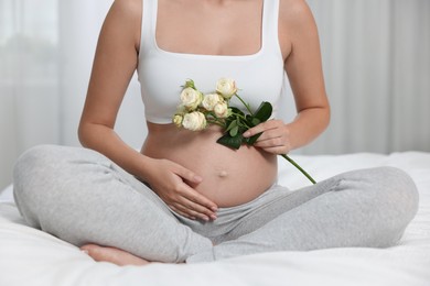 Photo of Pregnant woman with roses sitting on bed indoors, closeup