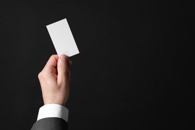 Photo of Businessman holding blank business card on black background, closeup. Space for text