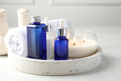 Spa composition. Bottles of cosmetic products, herbal bags, towel and burning candle on light table