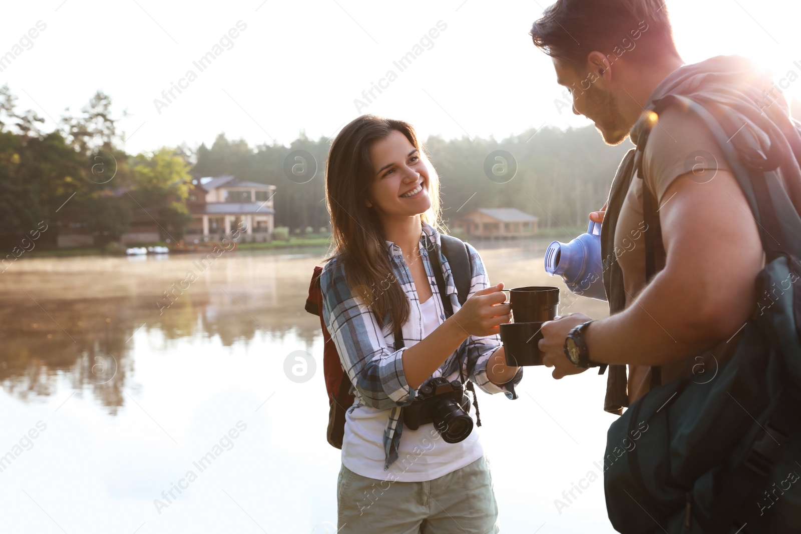 Photo of Man pouring drink into mug for young woman outdoors. Camping season