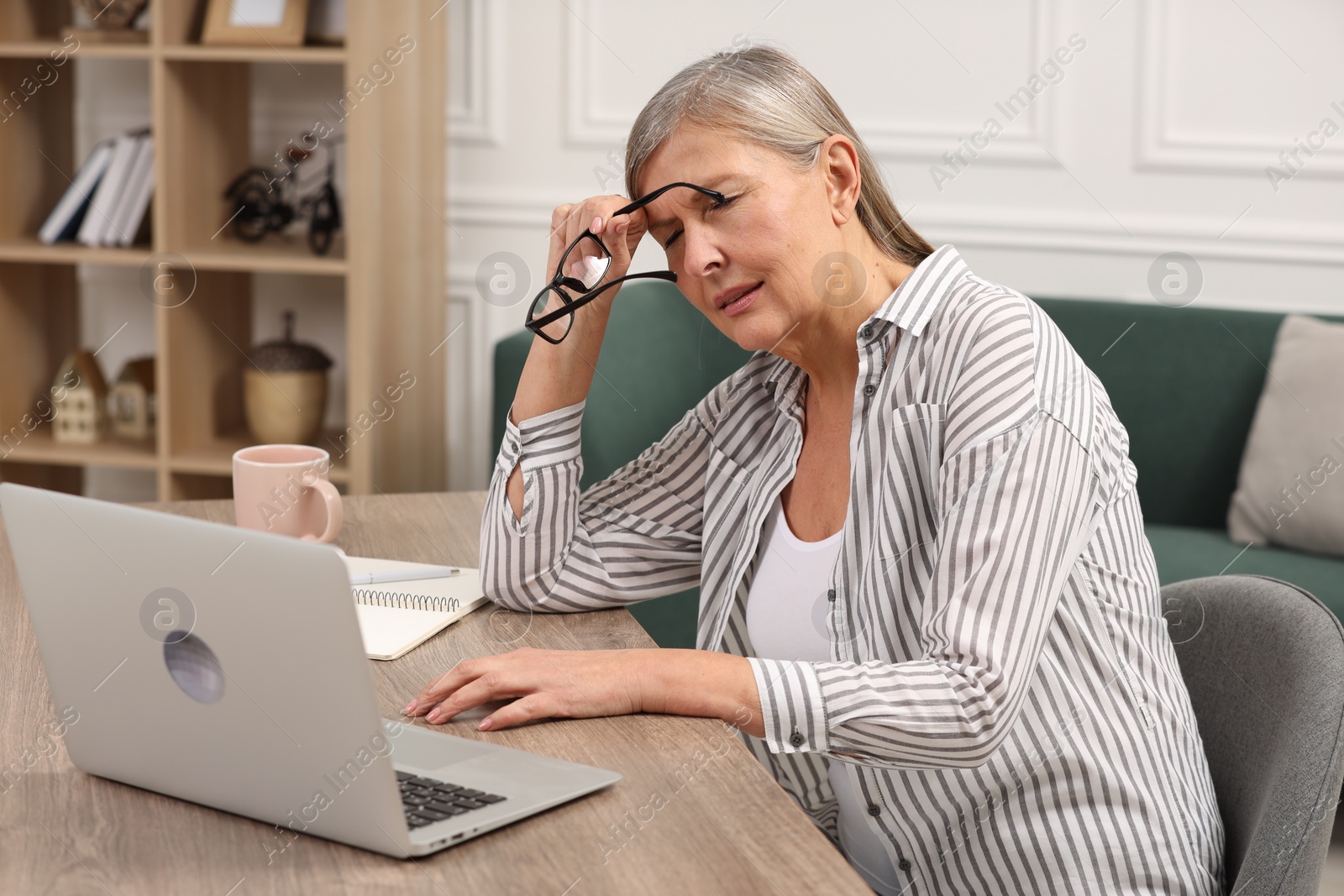 Photo of Menopause. Woman suffering from headache at wooden table indoors