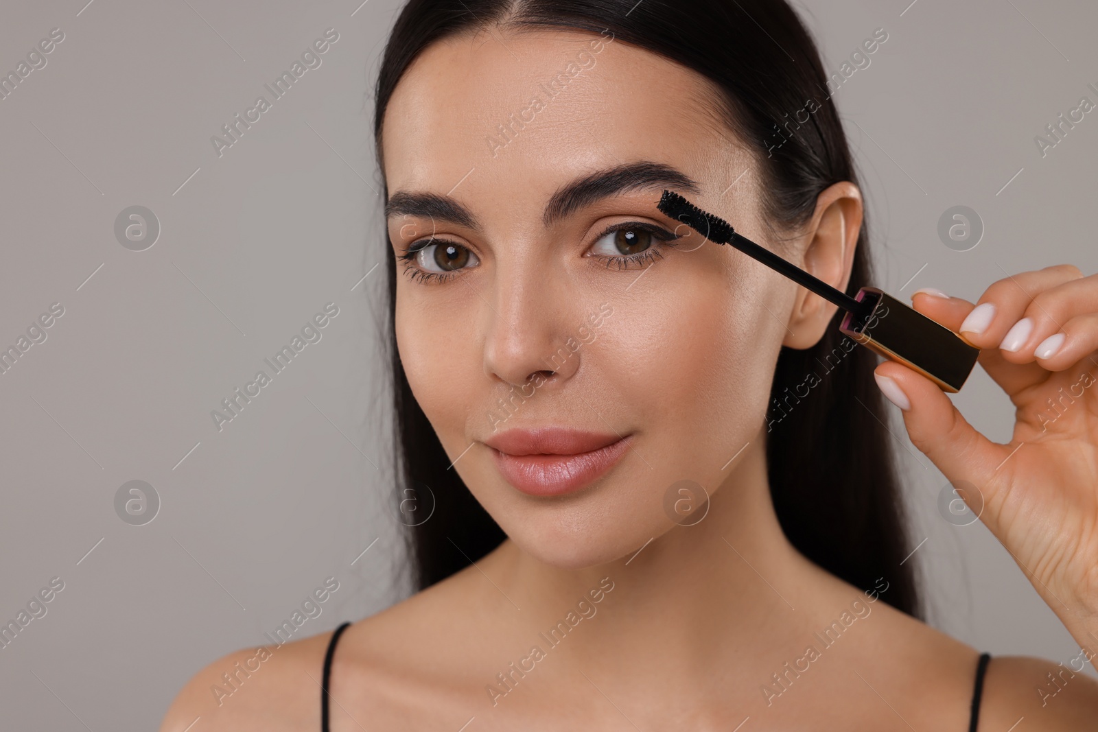 Photo of Beautiful young woman applying mascara on grey background, closeup