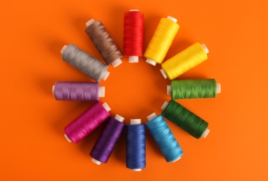 Photo of Different colorful sewing threads on orange background, flat lay. Space for text