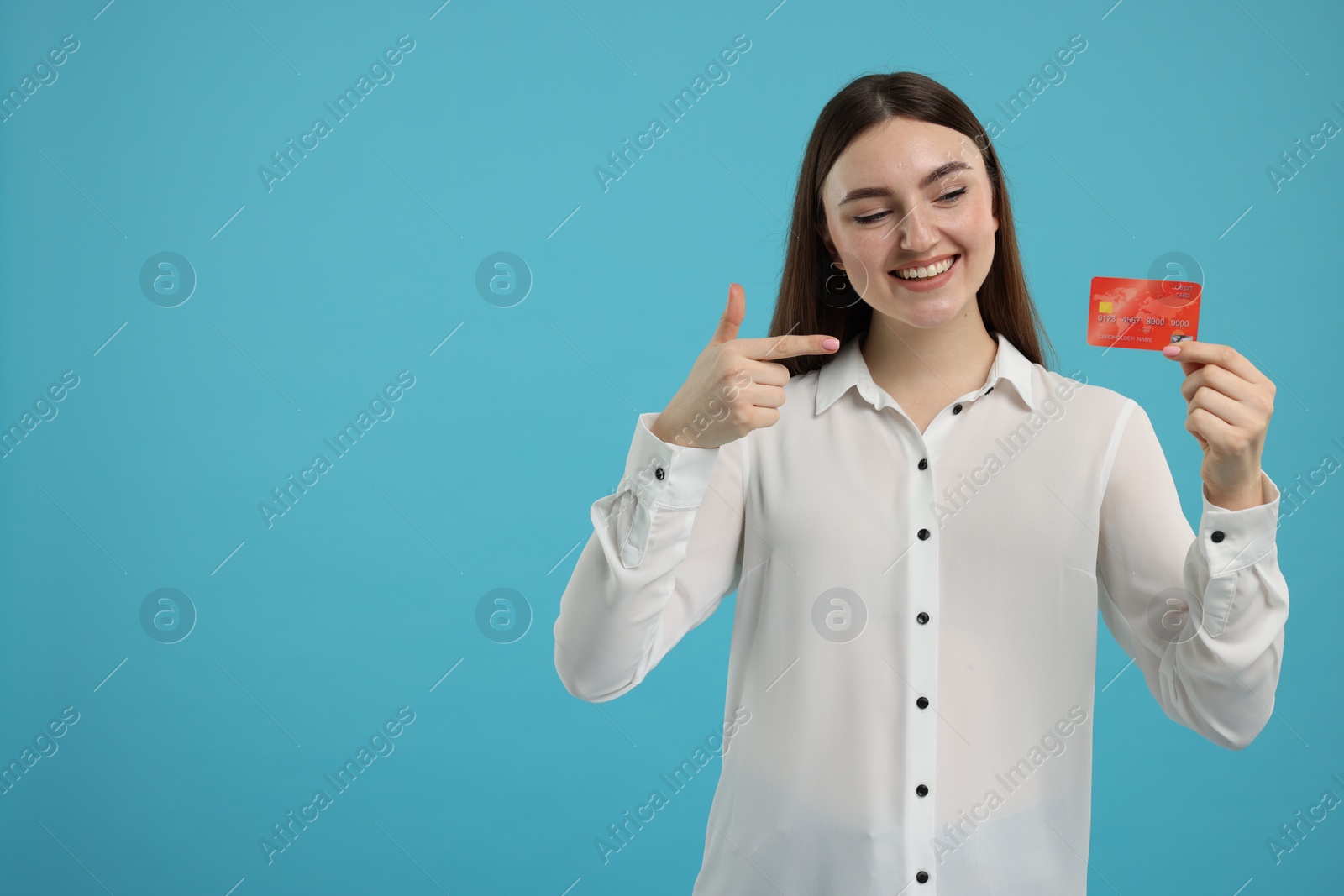 Photo of Happy woman pointing at credit card on light blue background, space for text