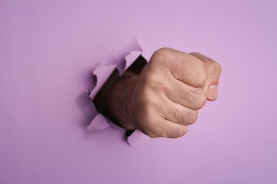 Photo of Man breaking through violet paper with fist, closeup