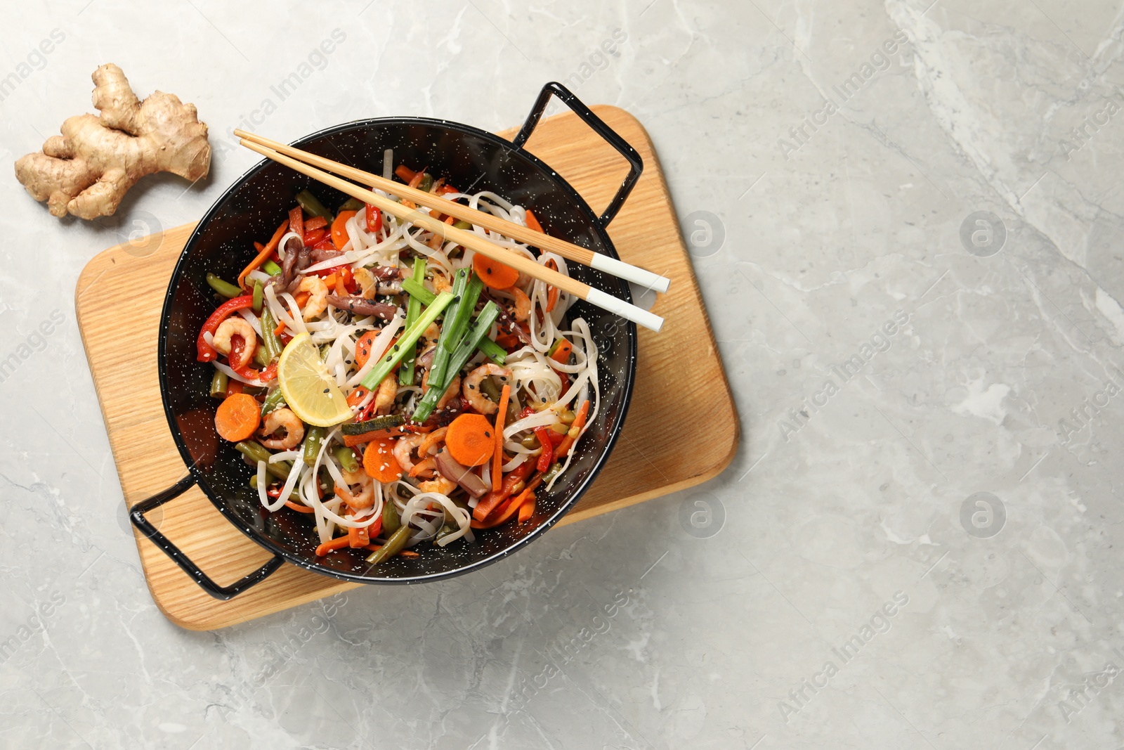 Photo of Shrimp stir fry with noodles and vegetables in wok on grey table, top view. Space for text