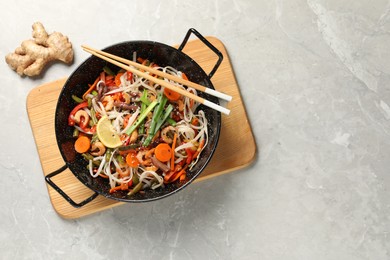 Photo of Shrimp stir fry with noodles and vegetables in wok on grey table, top view. Space for text