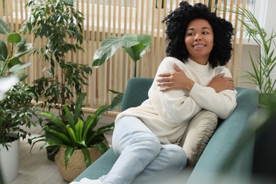 Photo of Happy woman relaxing on sofa near beautiful houseplants at home