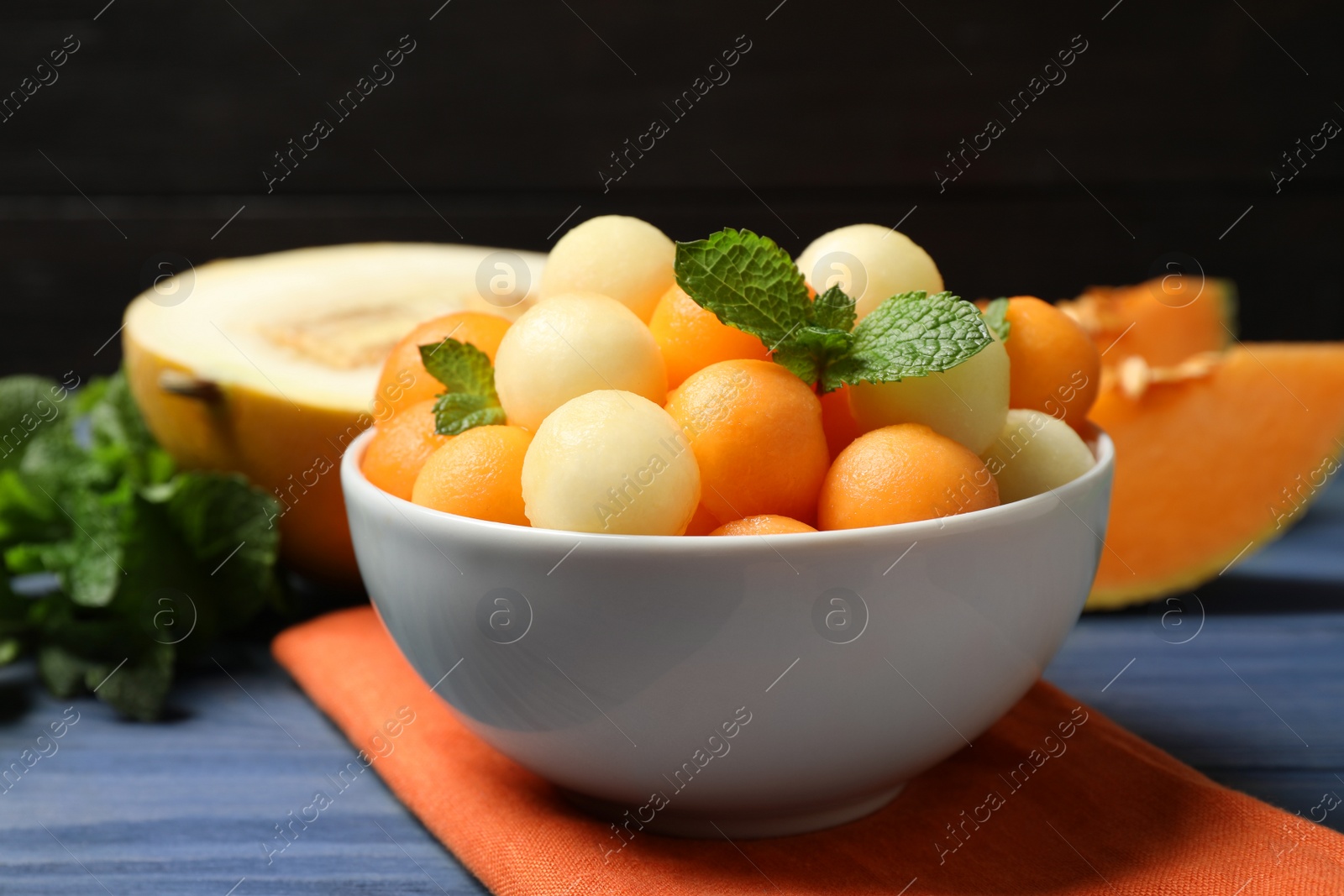 Photo of Melon balls and mint in bowl on blue wooden table, closeup