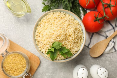 Photo of Delicious bulgur with parsley, dill, oil and tomatoes on light grey table, flat lay