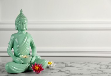 Photo of Buddha statue with burning candle and lotus flowers on white marble table. Space for text