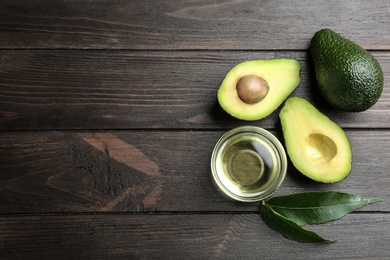 Photo of Bowl of natural oil and avocados on wooden background, flat lay. Space for text