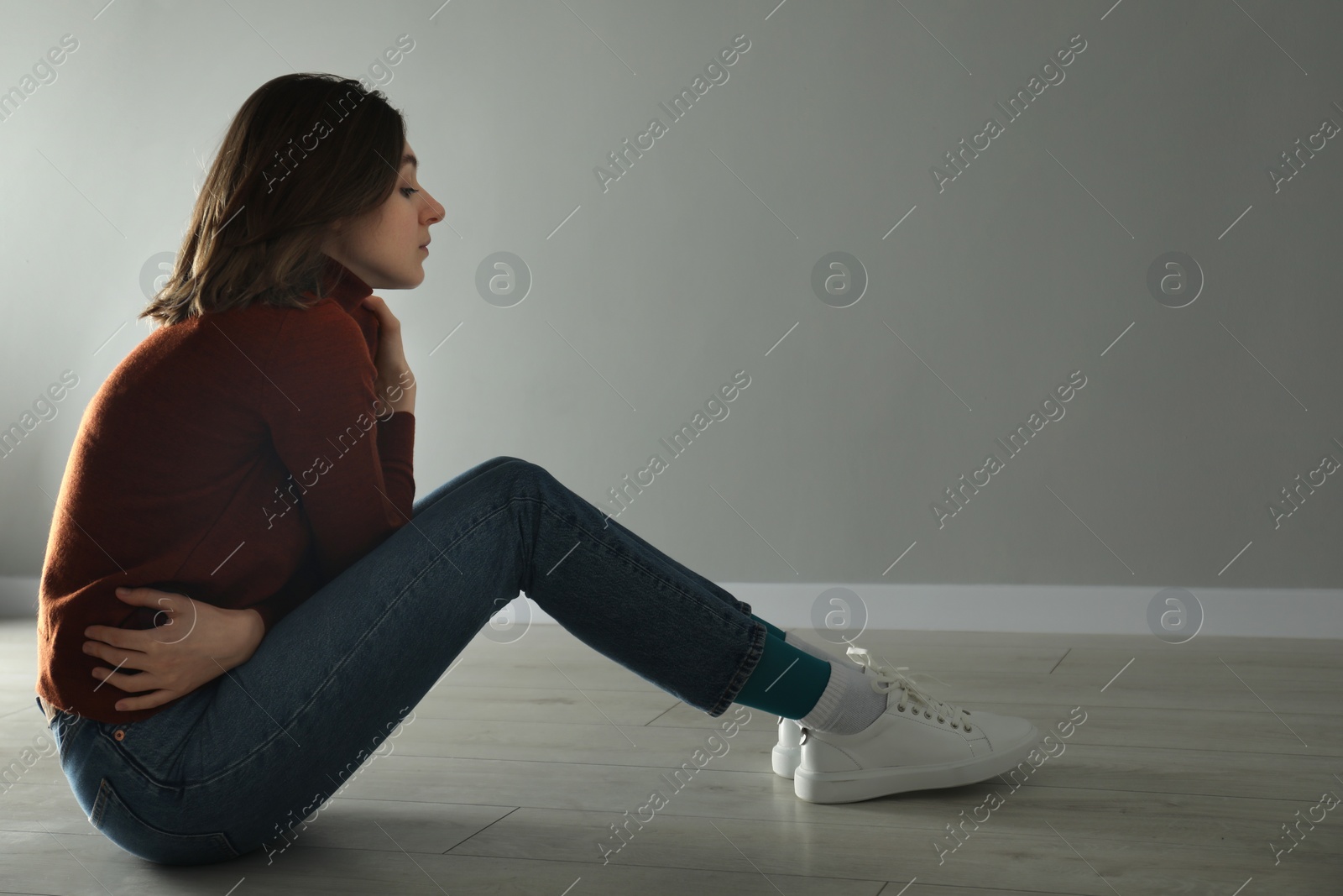 Photo of Sad young woman sitting on floor near grey wall indoors, space for text