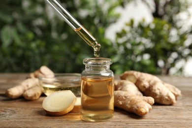 Dripping ginger essential oil from pipette into bottle on wooden table