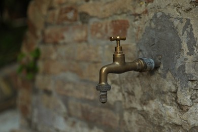 Metal water tap on old brick wall outdoors, closeup