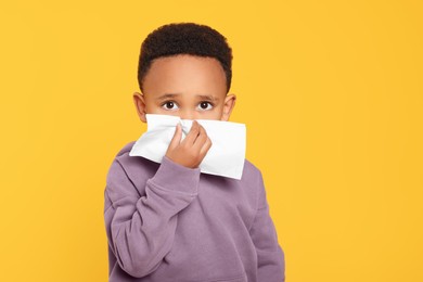 Photo of African-American boy blowing nose in tissue on yellow background. Cold symptoms
