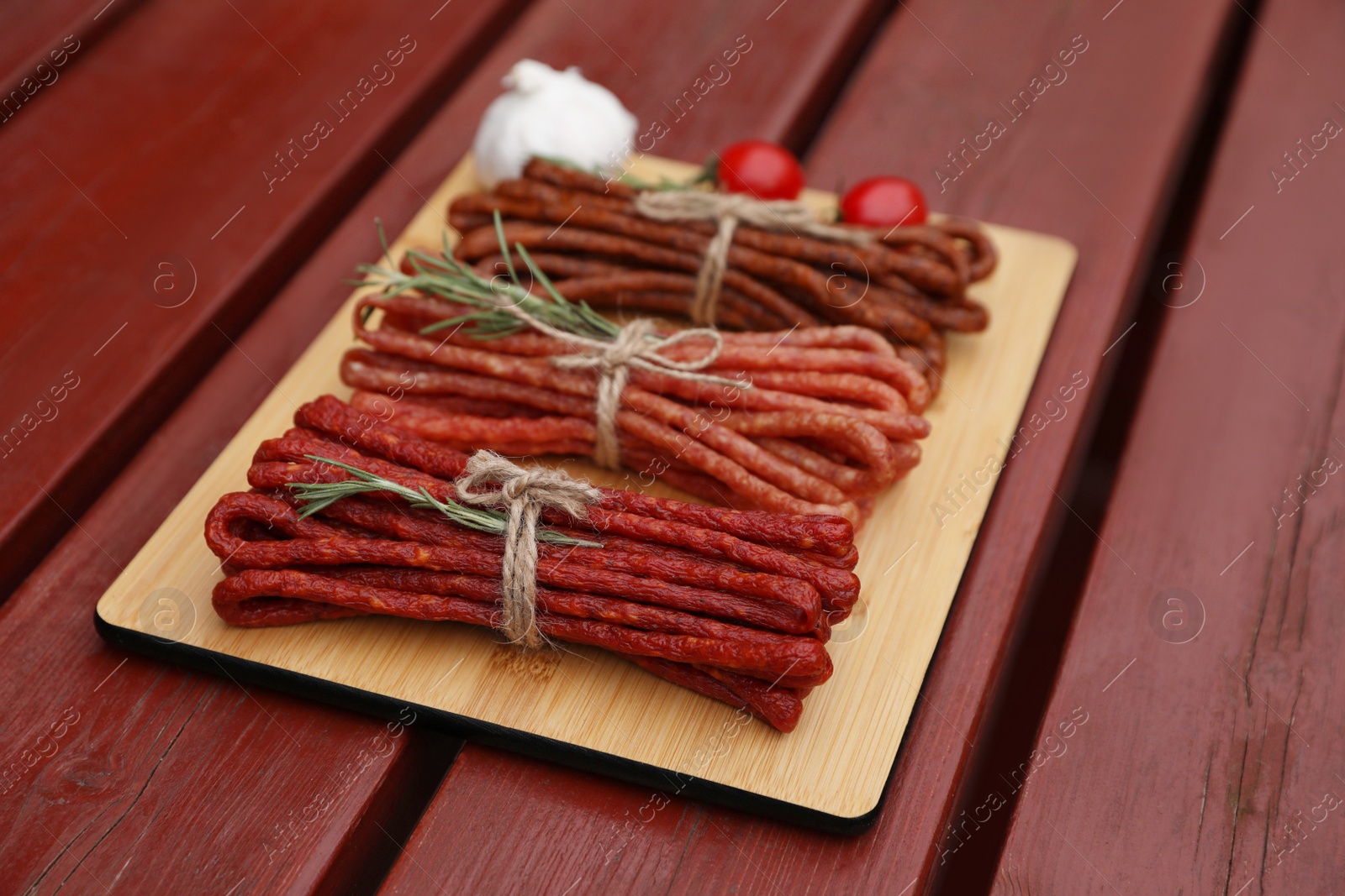 Photo of Bundles of delicious kabanosy with rosemary, tomatoes and garlic on wooden table