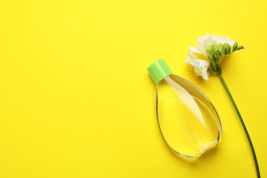 Photo of Bottle of baby oil and blooming freesia on yellow background, flat lay. Space for text