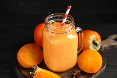 Photo of Tasty persimmon smoothie with straw and fresh fruits on black table