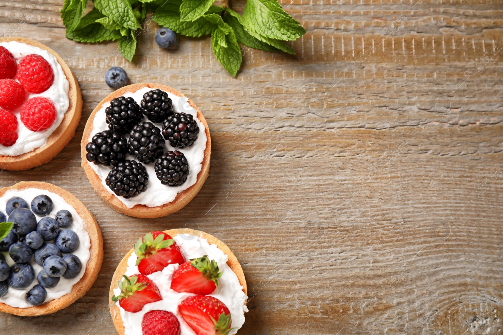 Photo of Different berry tarts on wooden table, flat lay with space for text. Delicious pastries