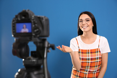 Photo of Young blogger recording video on camera against blue background