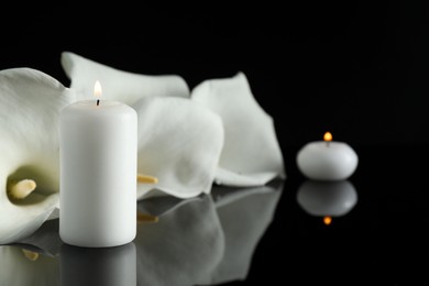 Photo of White calla lily flowers and burning candles on black mirror surface in darkness, closeup with space for text. Funeral symbols