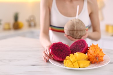 Young woman with fresh exotic fruits at table in kitchen, closeup. Space for text