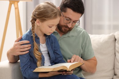 Photo of Girl and her godparent reading Bible together on sofa at home