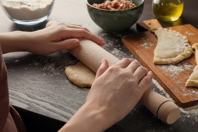Photo of Woman rolling dough for chebureki at wooden table, closeup