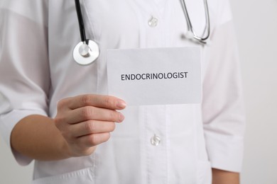 Image of Endocrinologist with stethoscope holding card on light grey background, closeup