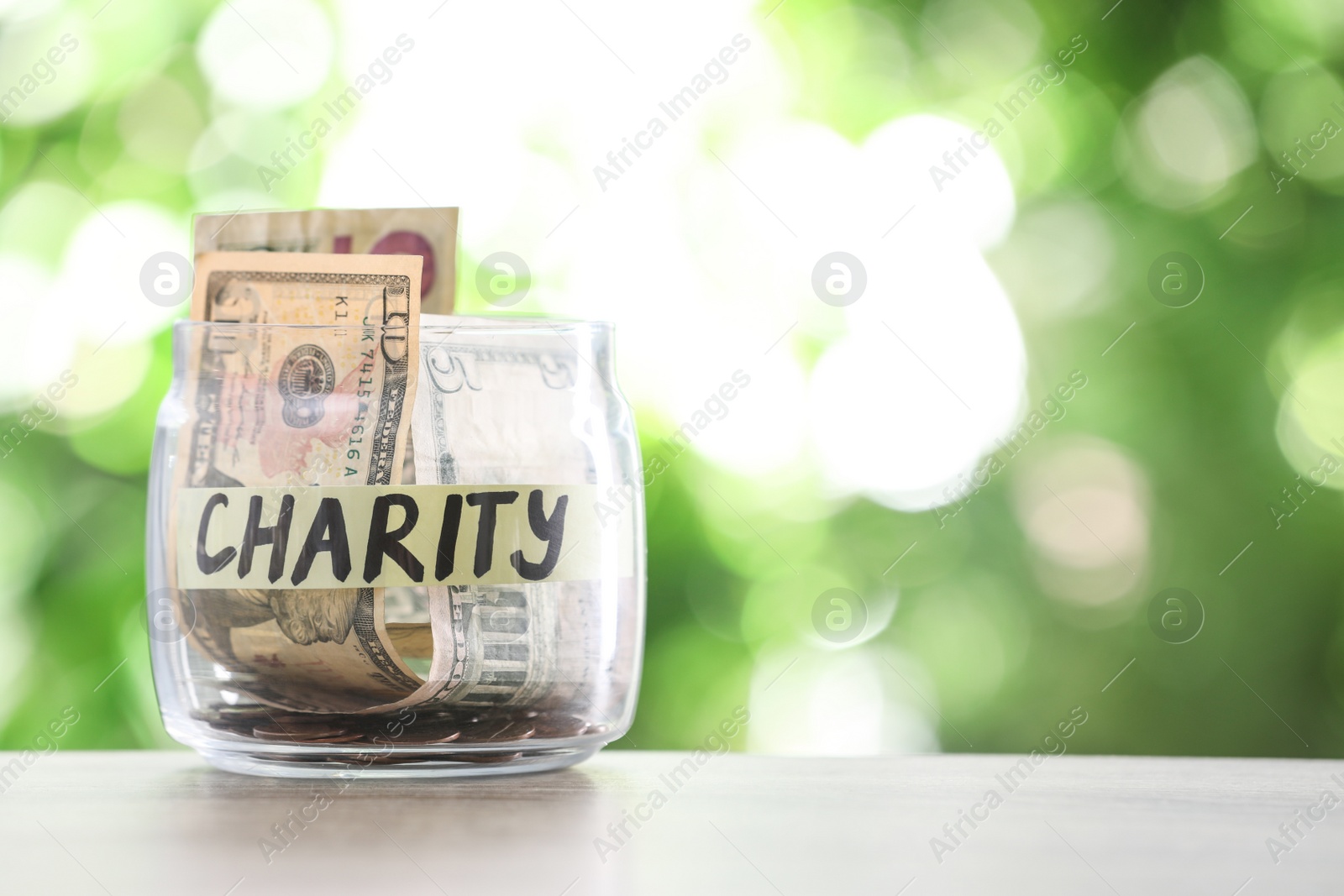 Photo of Glass jar with money and label CHARITY on table against blurred background. Space for text