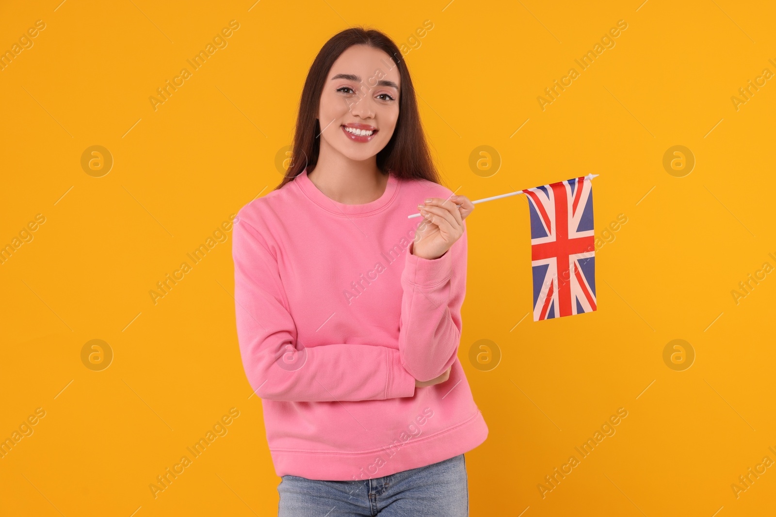 Photo of Young woman holding flag of United Kingdom on orange background