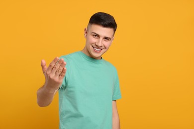 Photo of Handsome man inviting to come in against orange background