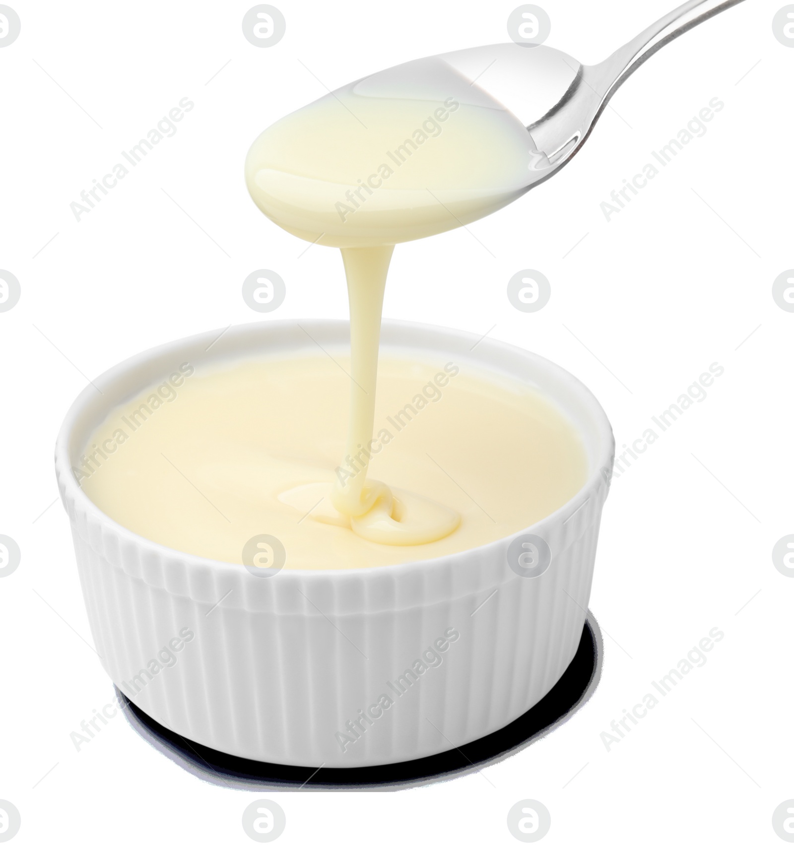 Photo of Condensed milk flowing down from spoon into bowl isolated on white