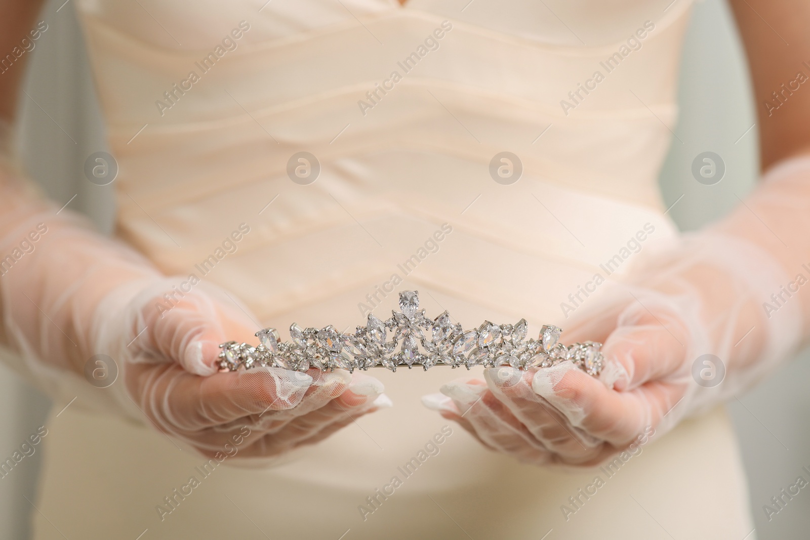 Photo of Bride holding luxurious tiara on grey background, closeup view