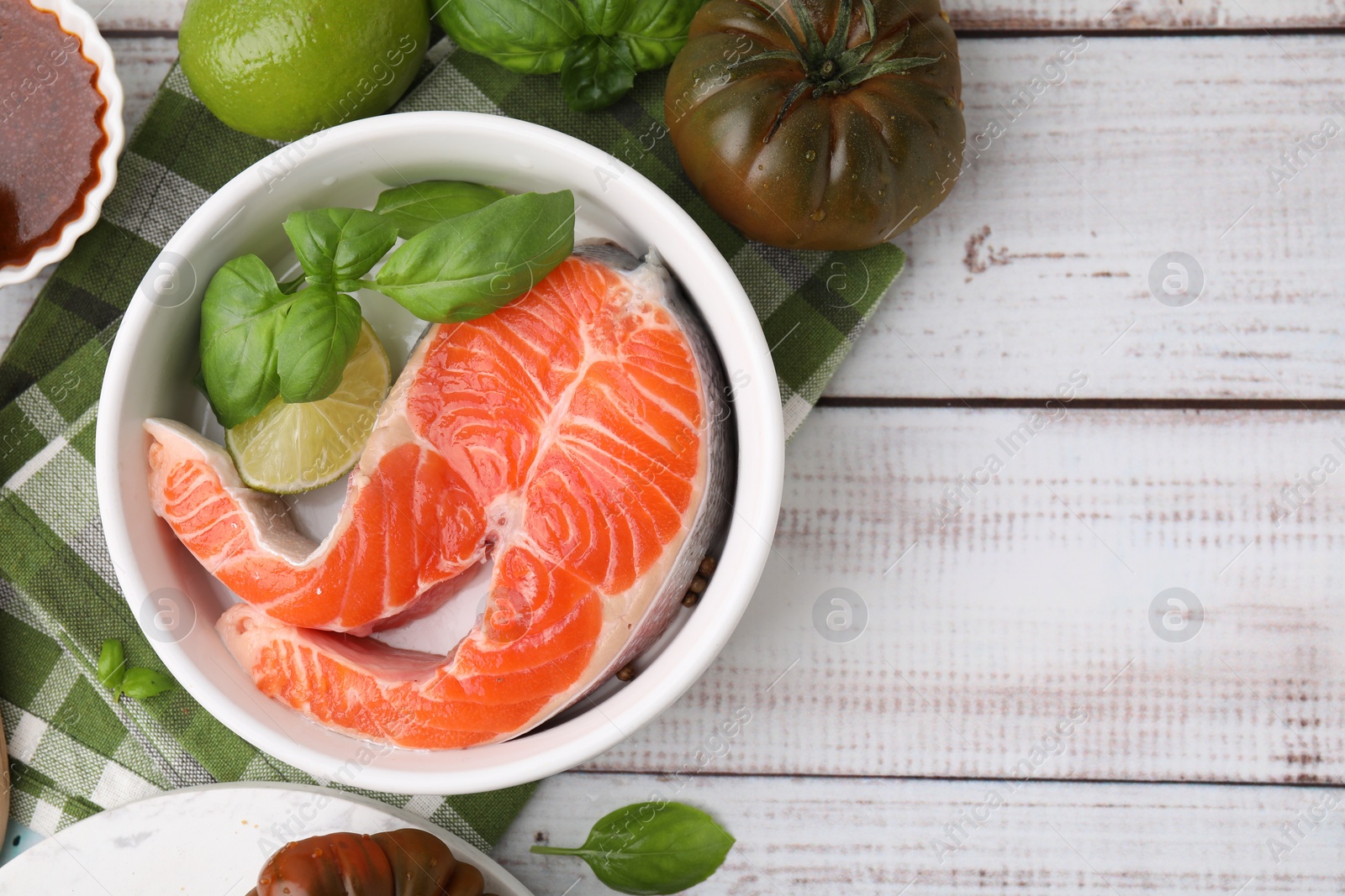 Photo of Fresh marinated fish, lime and other products on white wooden table, flat lay. Space for text